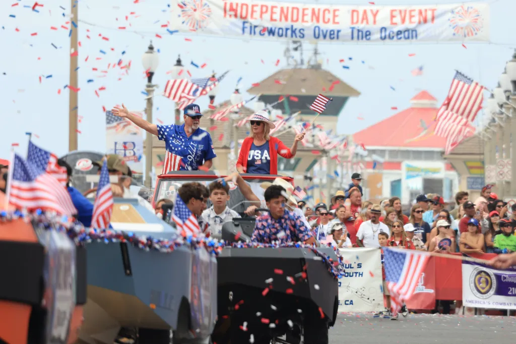 Spectators and parade participants celebrate Huntington Beach's 122nd Annual Fourth of July parade with red, white, and blue confetti and attire.