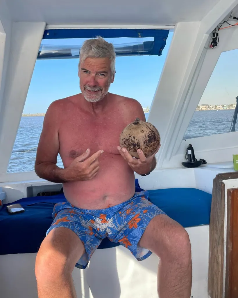 Brian Hooker holding a coconut and pointing to his stomach on a boat.