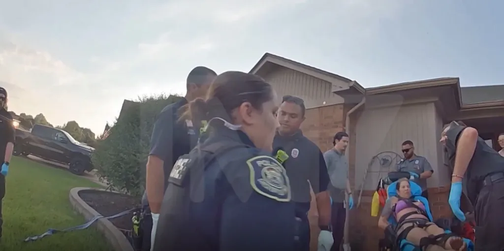 Kim Mathers on a stretcher outside a home, surrounded by emergency personnel.