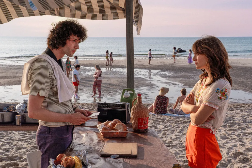 Dominic Sessa and Emilia Jones stand on a beach at sunset.