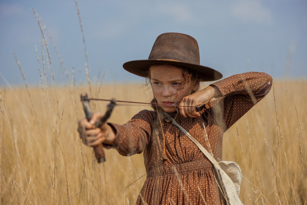 Alice Halsey as Laura Ingalls aiming a slingshot in a field.