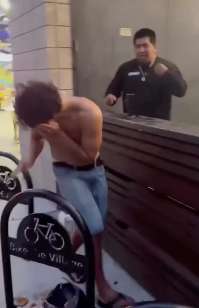 A shirtless man in jeans covering his face after being tased by a bouncer.