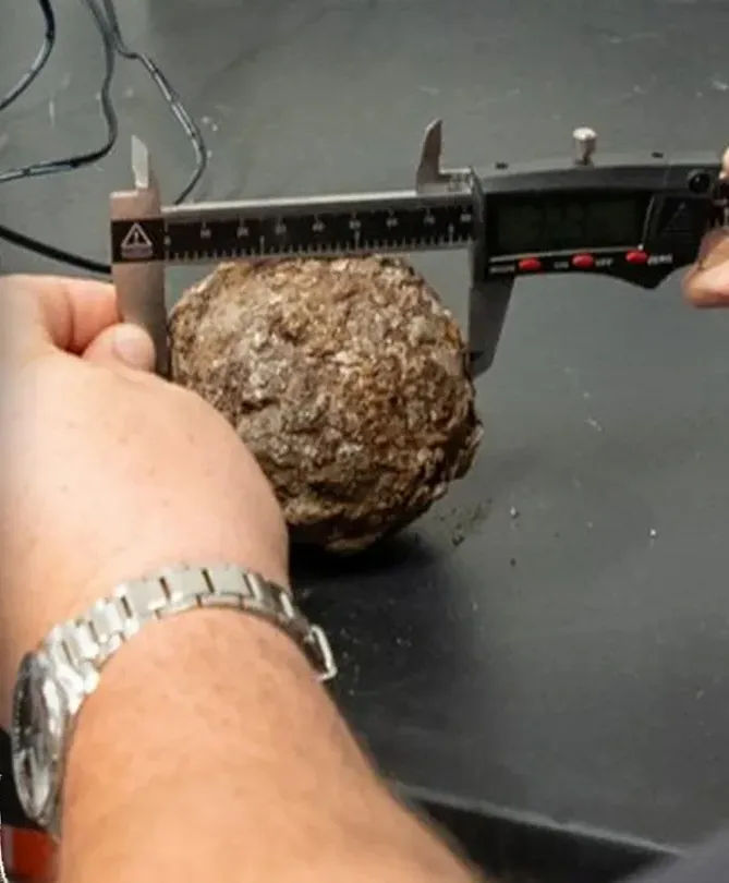 A hand measures a cannonball with digital calipers.