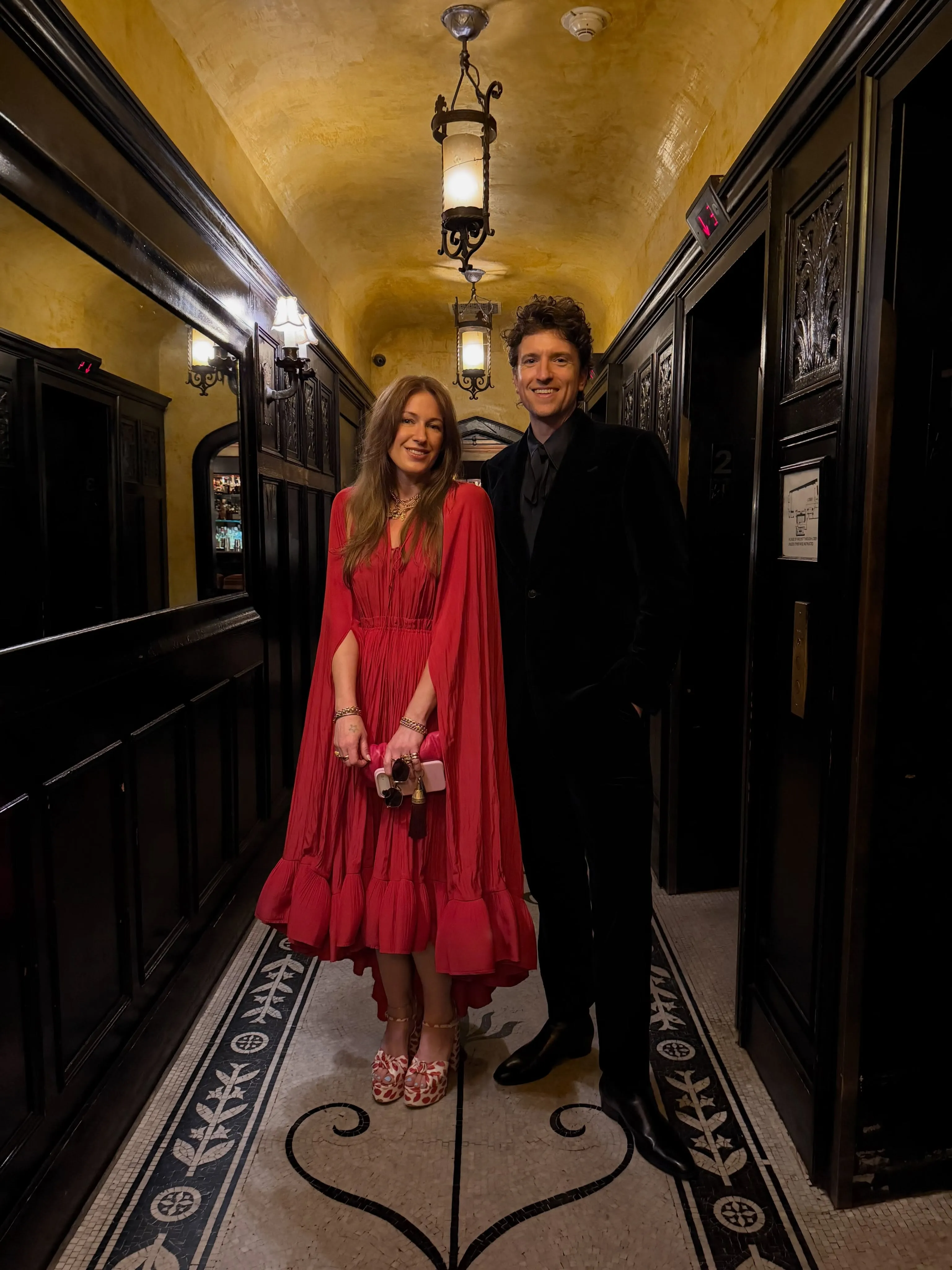 Greg James with his wife, Bella, posing in a well-lit hallway.