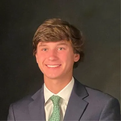 Photo of James "Walter" Hensley, a young man with brown hair and a white shirt and green tie, smiling against a dark background.