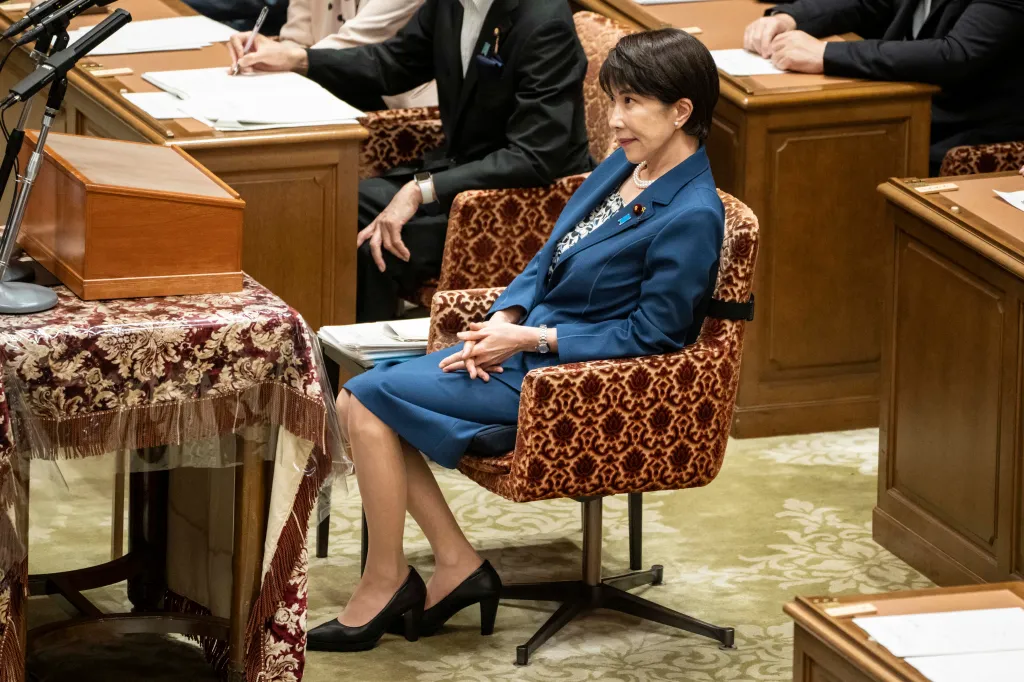 Japanese Prime Minister Sanae Takaichi sits in a patterned chair, wearing a blue suit and pearl necklace, at the National Diet in Tokyo.