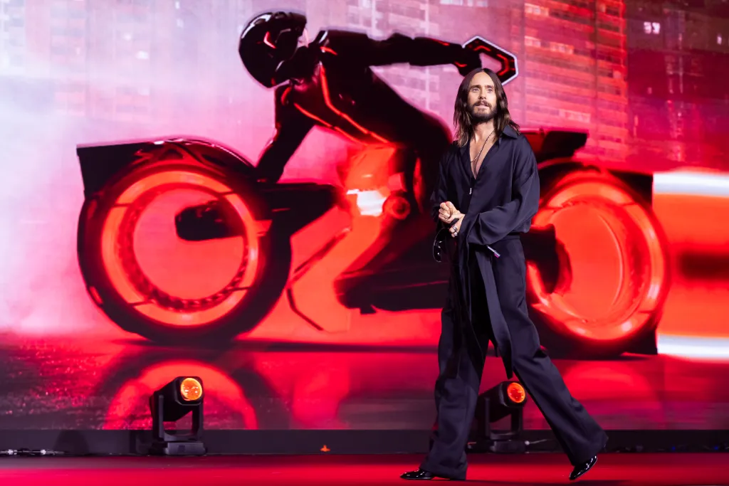 Jared Leto on stage at the San Diego Comic-Con Malaga 2025 in front of a Tron Ares motorcycle background.