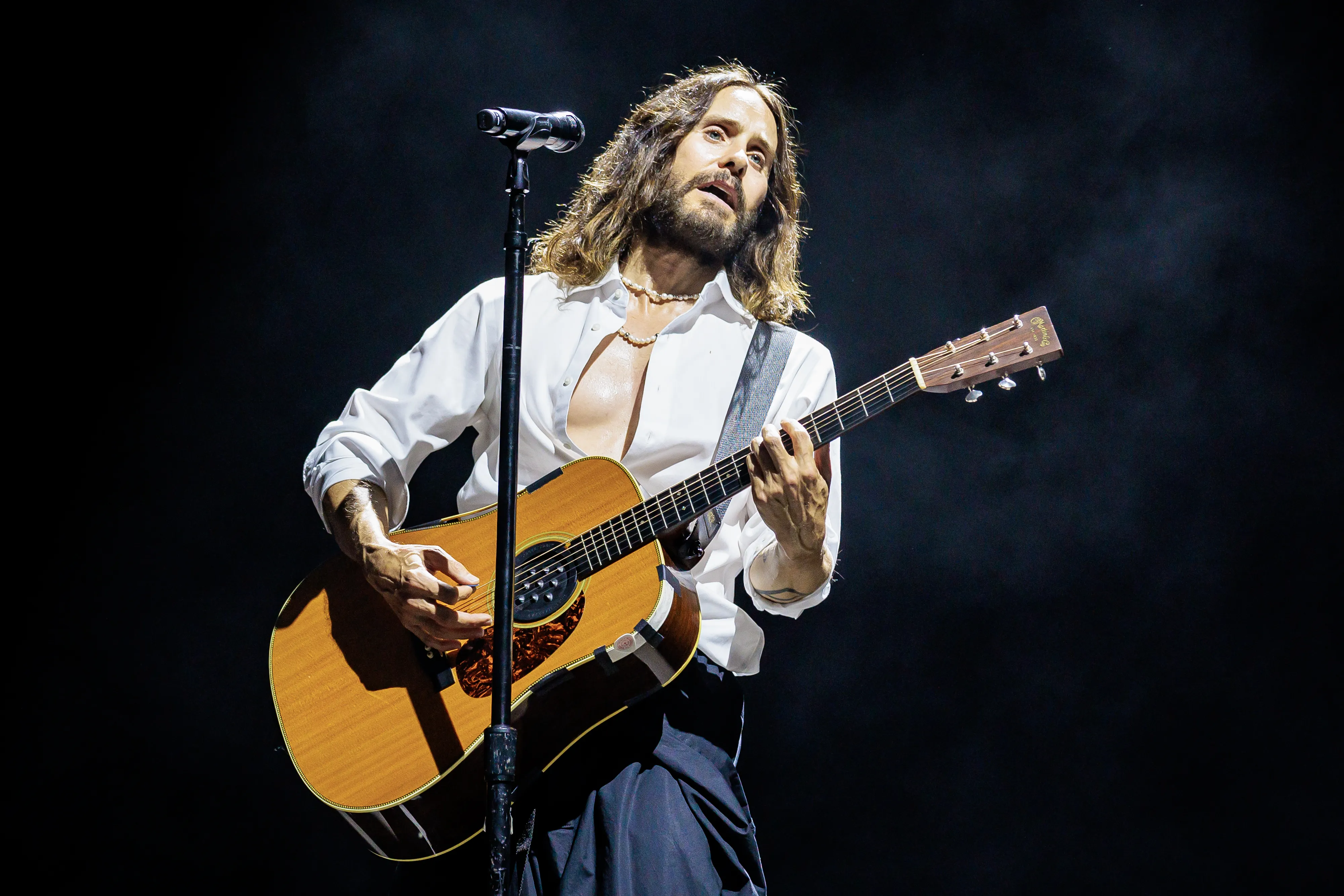Jared Leto of Thirty Seconds To Mars performing on stage with an acoustic guitar.