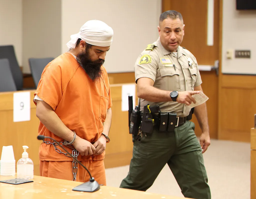 Jashanpreet Singh, in an orange jumpsuit and handcuffs, stands beside a sheriff's deputy in a courtroom.