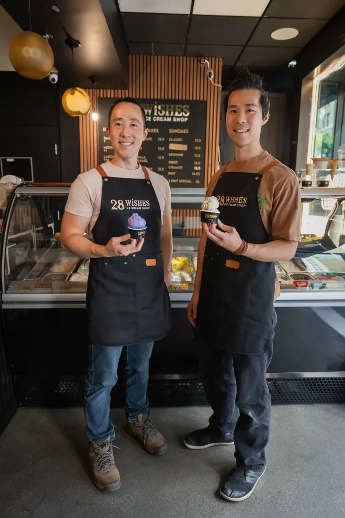 Jason Jiang and James Jiangon, brothers and owners of 28 Wishes Ice Cream Shop, stand in their shop holding ice cream cups.