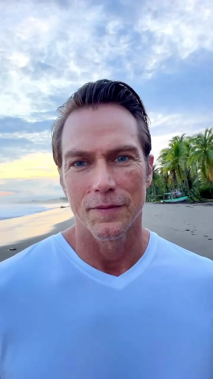 Jason L Lewis on a beach with palm trees at sunset.