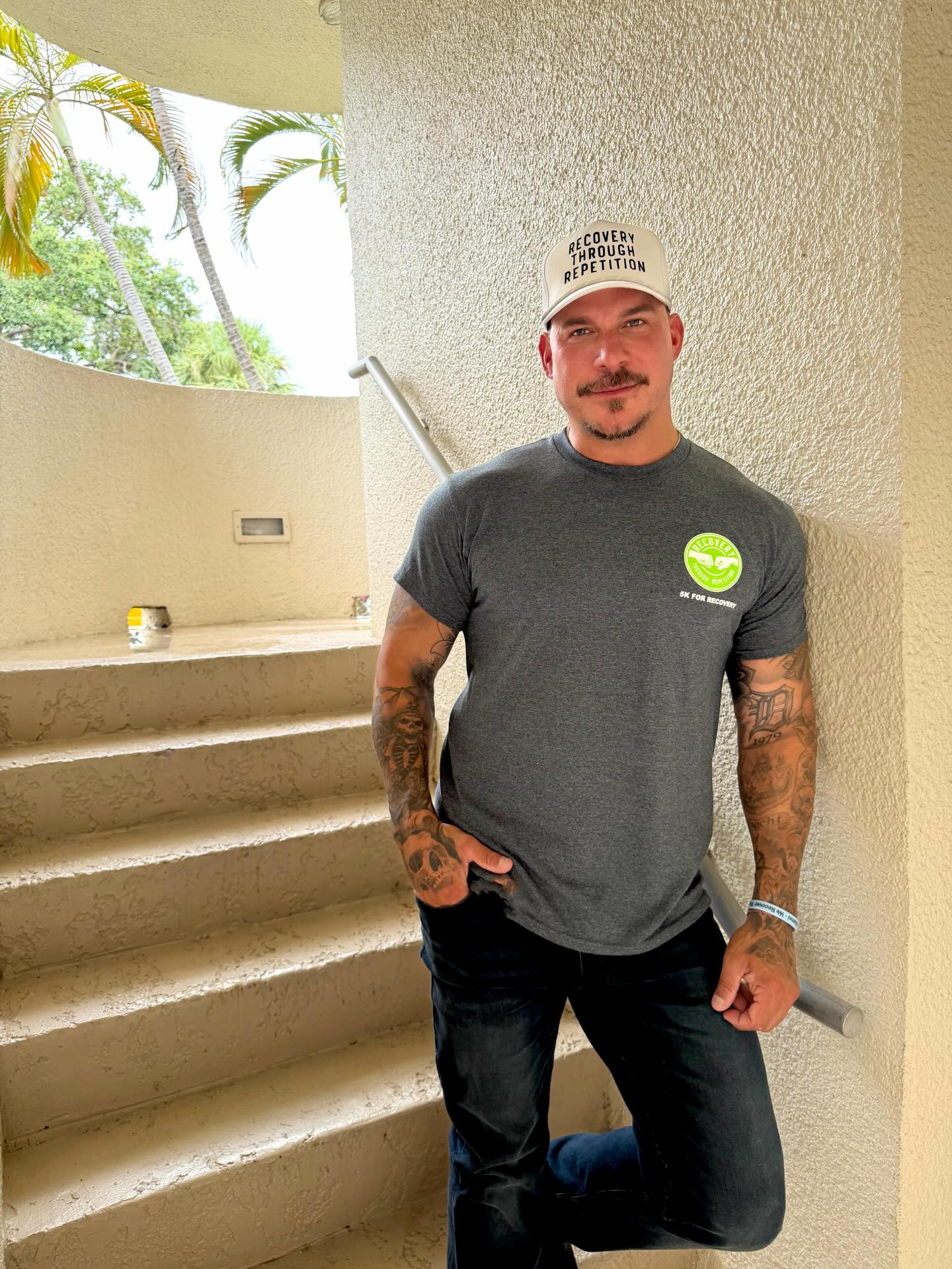 Jax Taylor in a gray t-shirt and a white hat that says "RECOVERY THROUGH REPETITION."