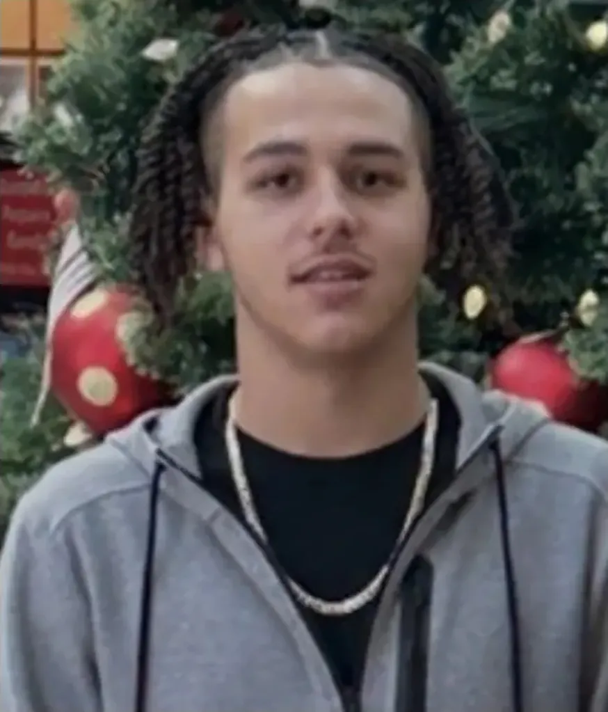 Jayden McComber, 18, wearing a gray hoodie and chain necklace, in front of a Christmas tree.