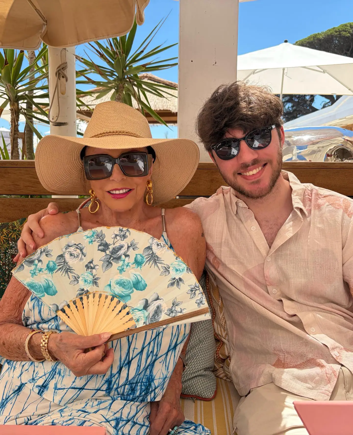 Joan Collins and Alison Papworth smiling together at a tropical outdoor setting.