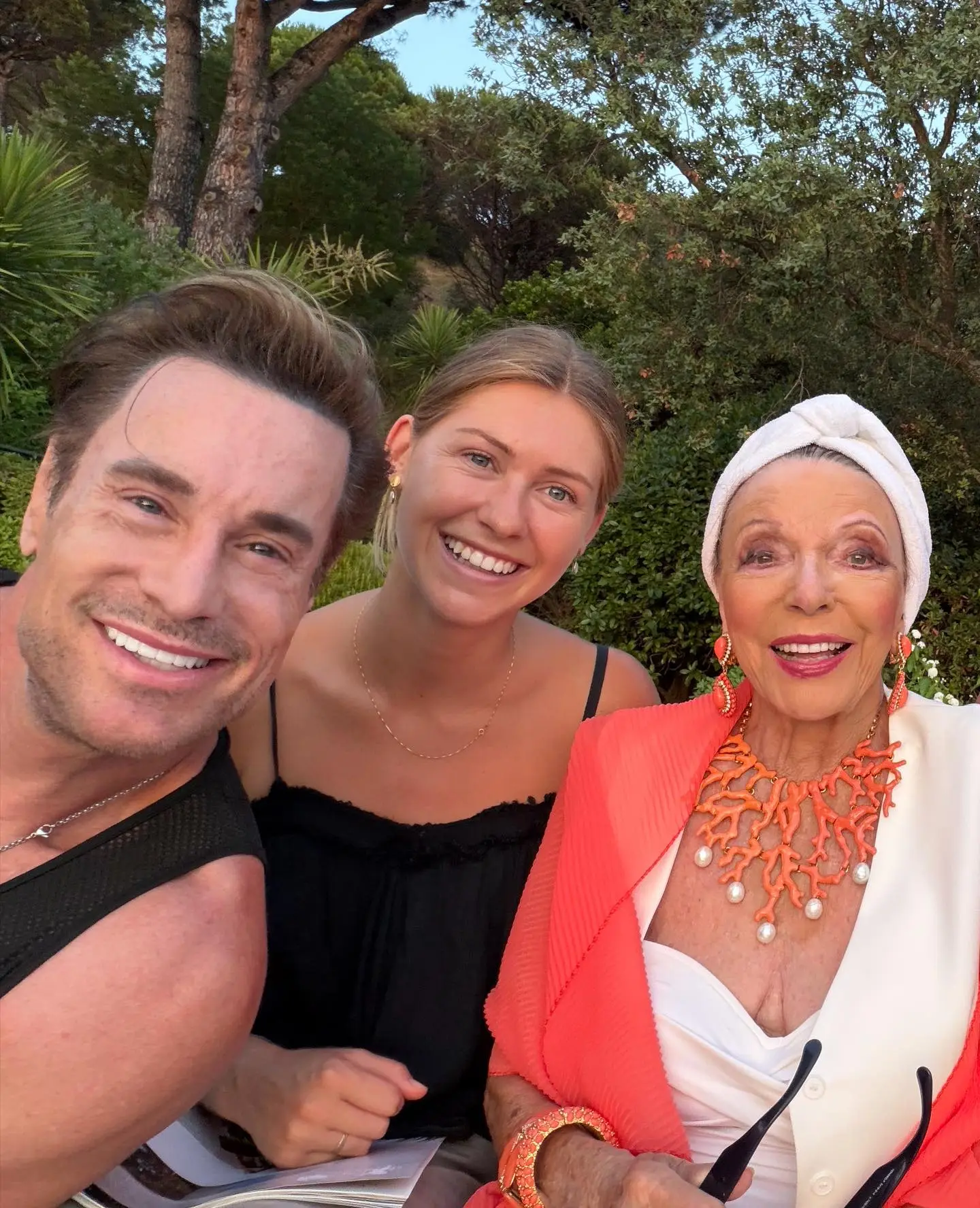 Joan Collins, Alison Papworth, and a man smiling for a selfie outdoors.