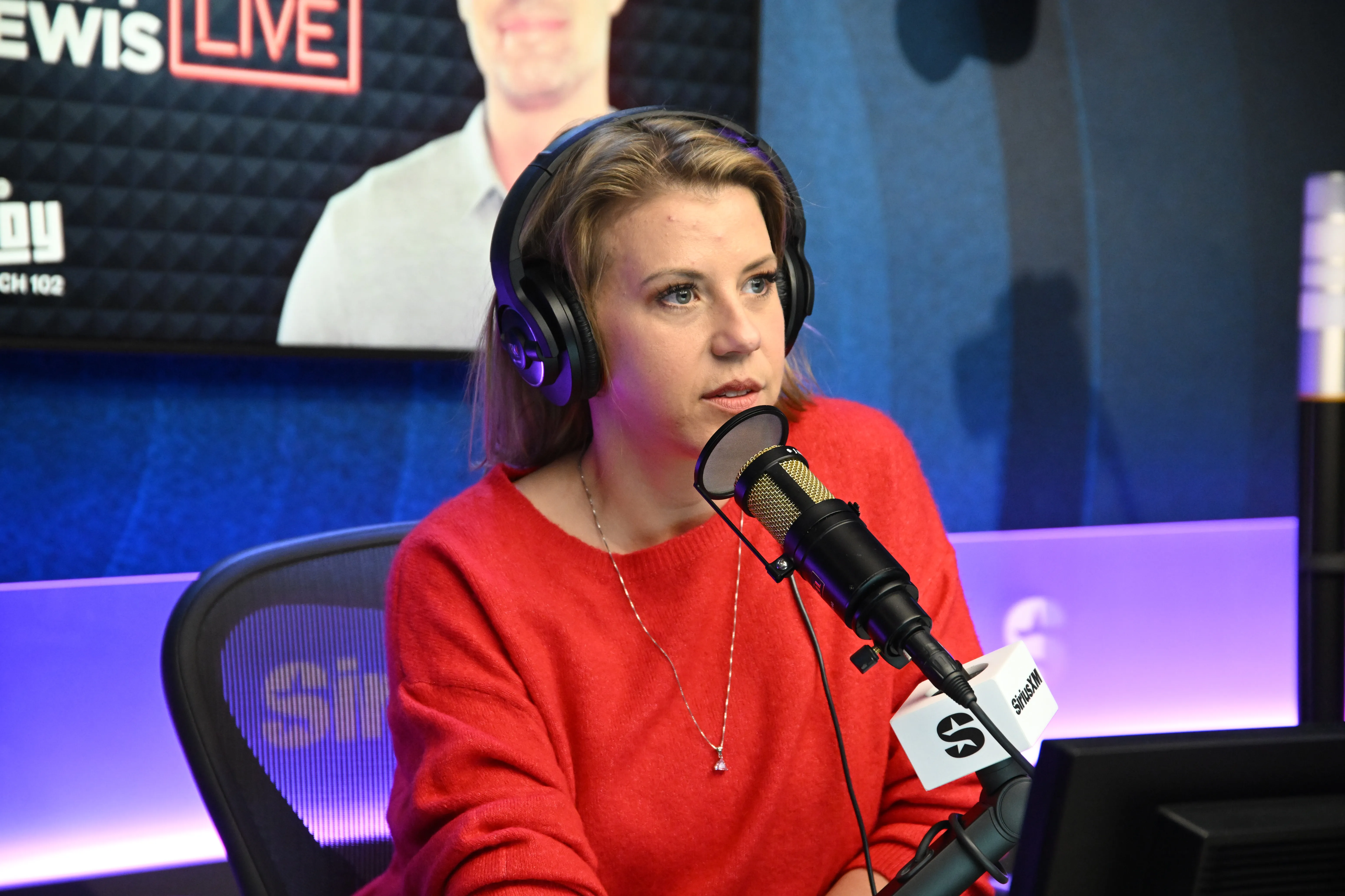 Jodie Sweetin wearing headphones and speaking into a microphone at SiriusXM Studios.