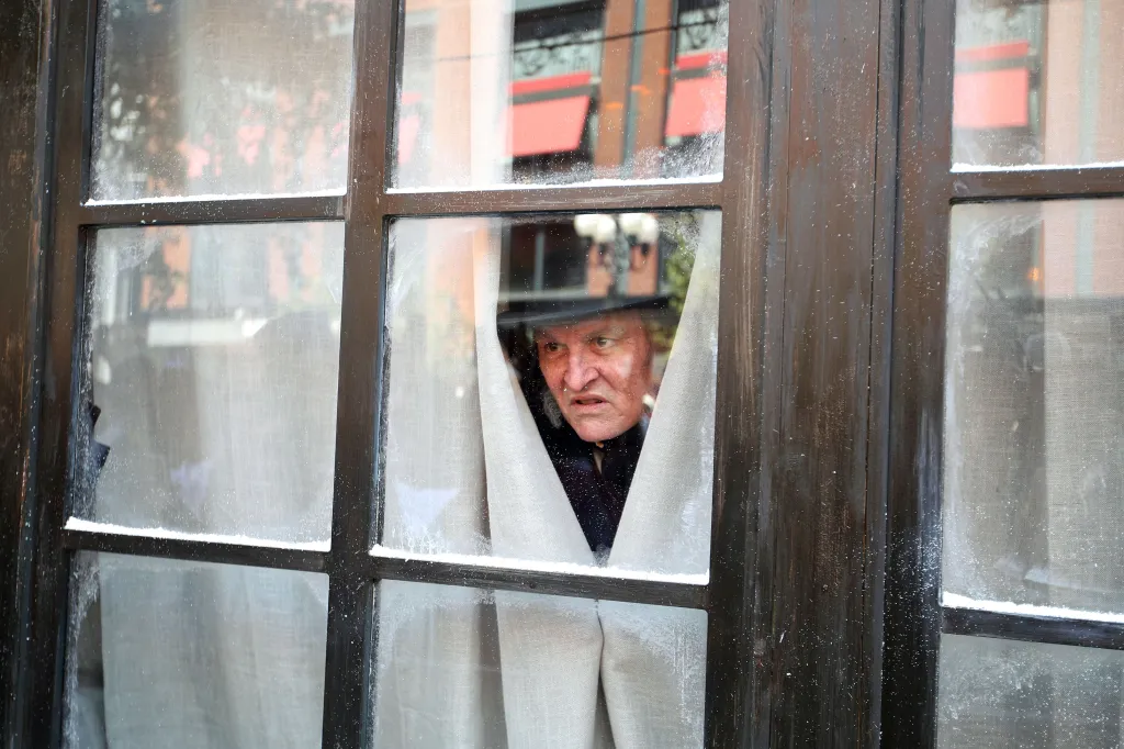Johnny Depp as Ebenezer Scrooge looking through a window with white curtains.