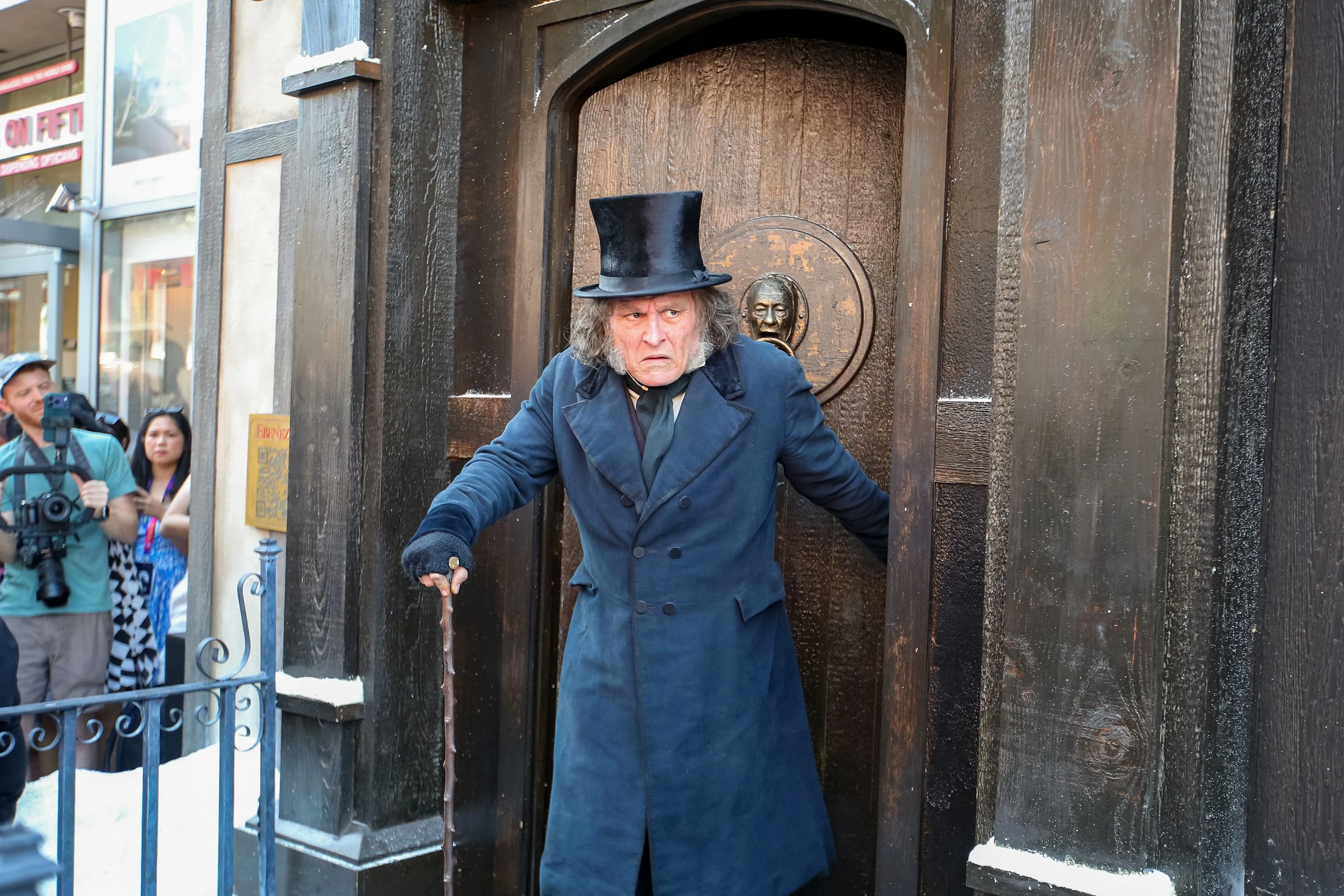 Johnny Depp, dressed as Ebenezer Scrooge, emerging from a doorway with a cane.