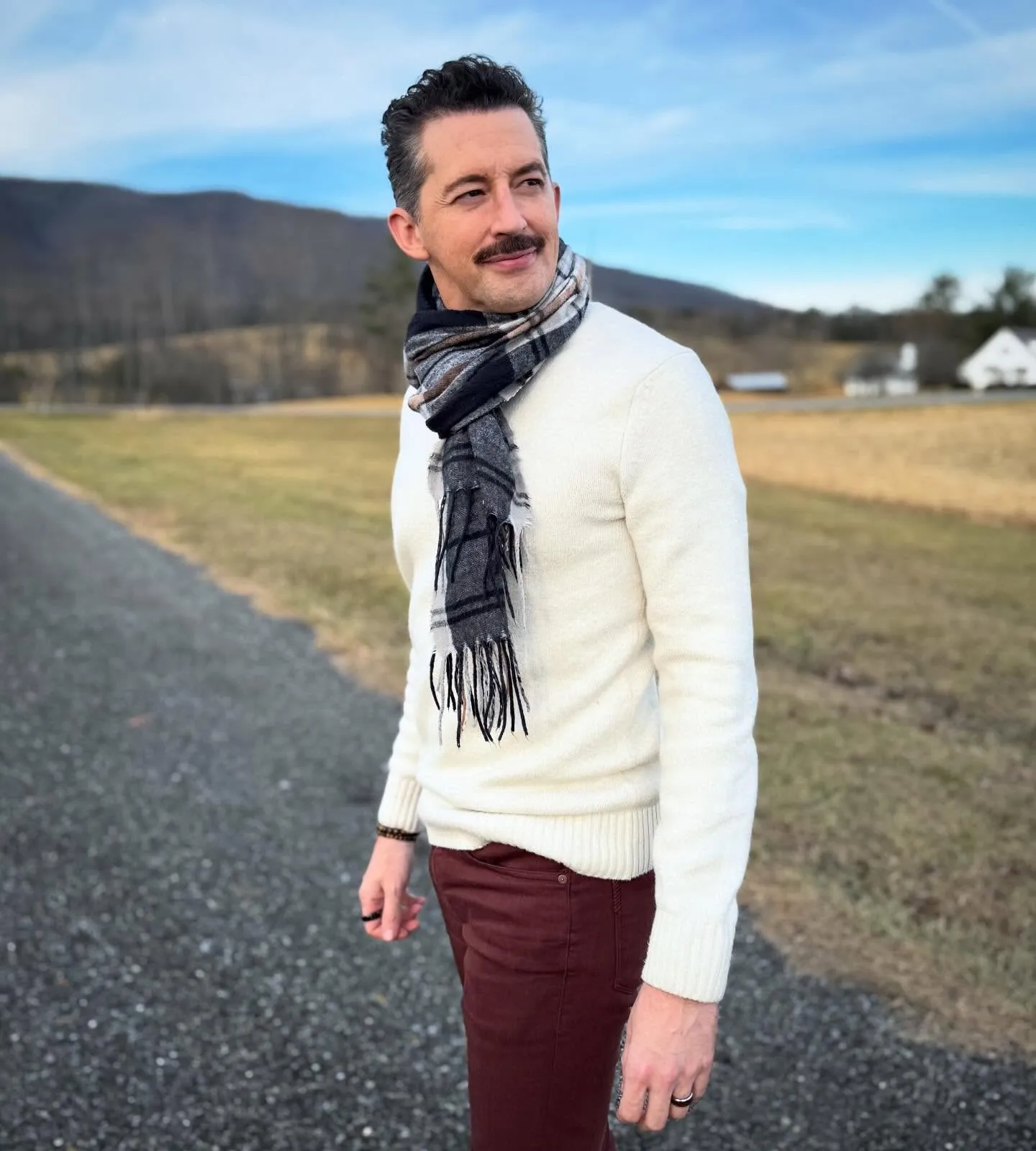 Josh Grisetti looking away from the camera, wearing a sweater and scarf, with mountains in the background.