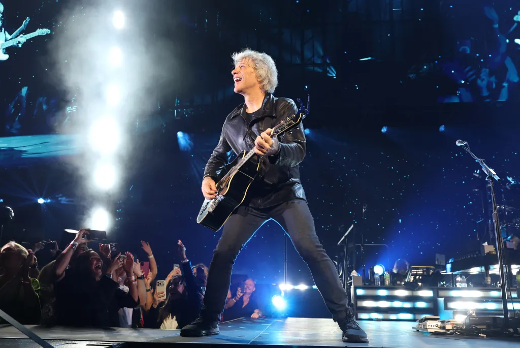 Jon Bon Jovi performs on stage with an acoustic guitar.
