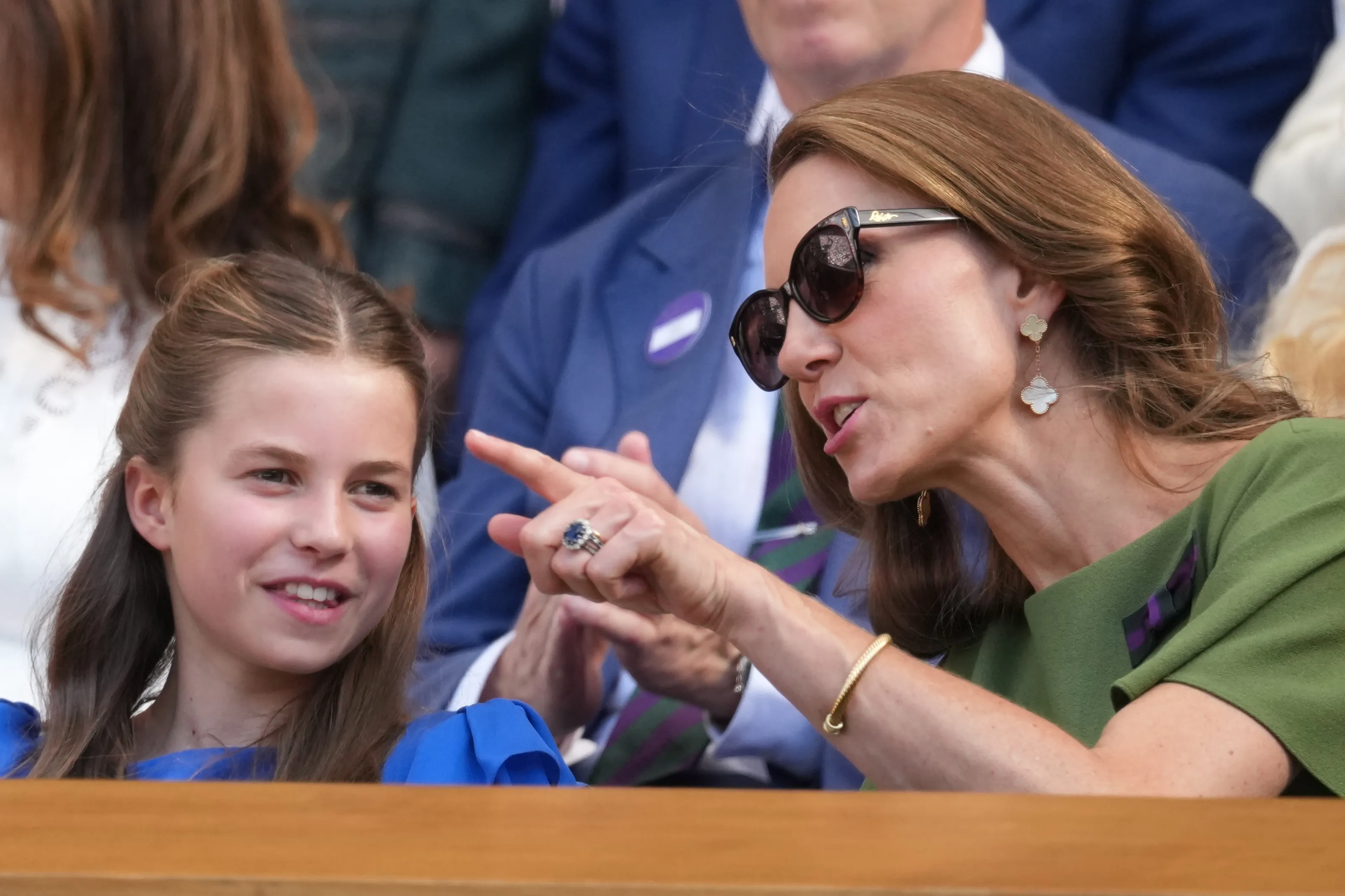 Princess Charlotte smiling beside her mother, Kate, Princess of Wales, who is wearing sunglasses and pointing.