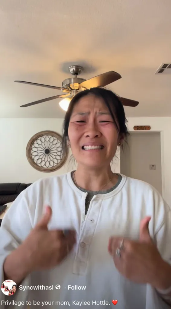 A woman grimaces with tears in her eyes, hands up as if in distress.