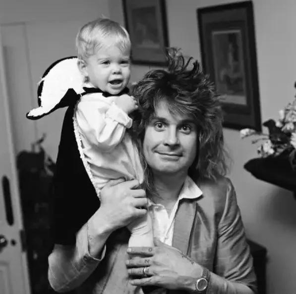 Ozzy Osbourne holds his young child on his shoulders.
