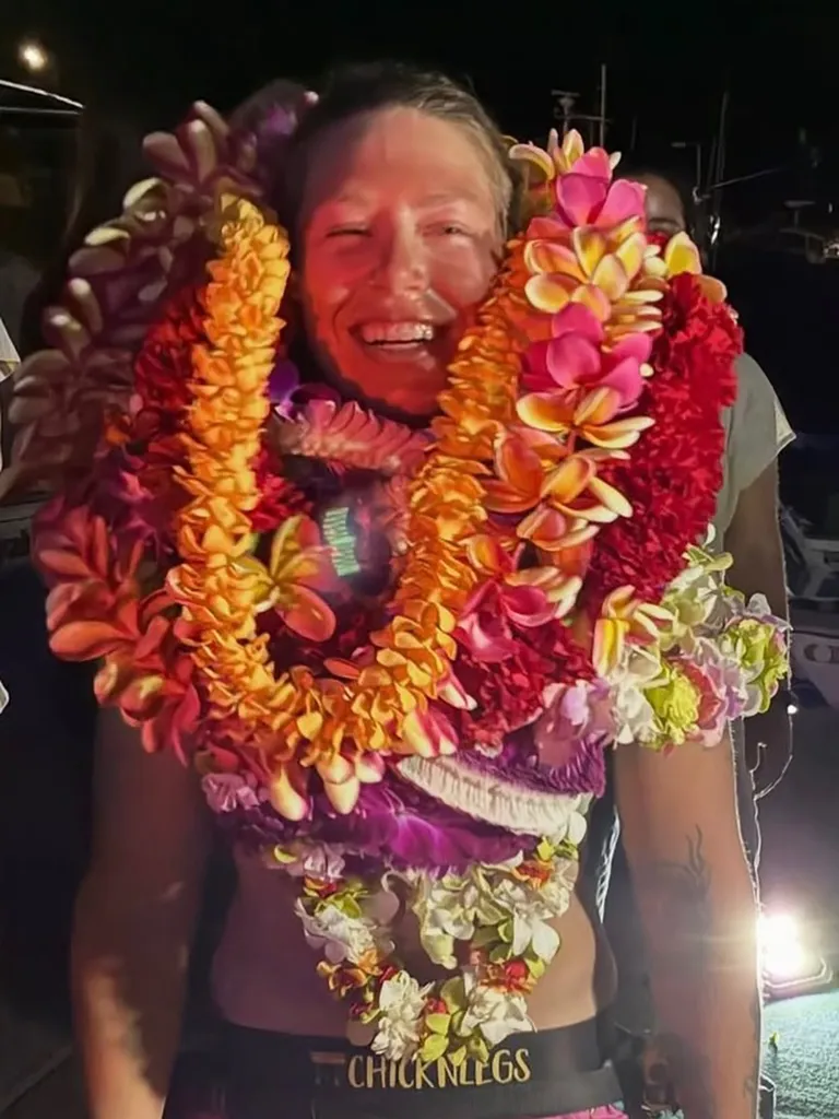 Kelsey Pfendler laughing, wearing numerous flower leis around her neck and torso after completing her solo rowing trip.