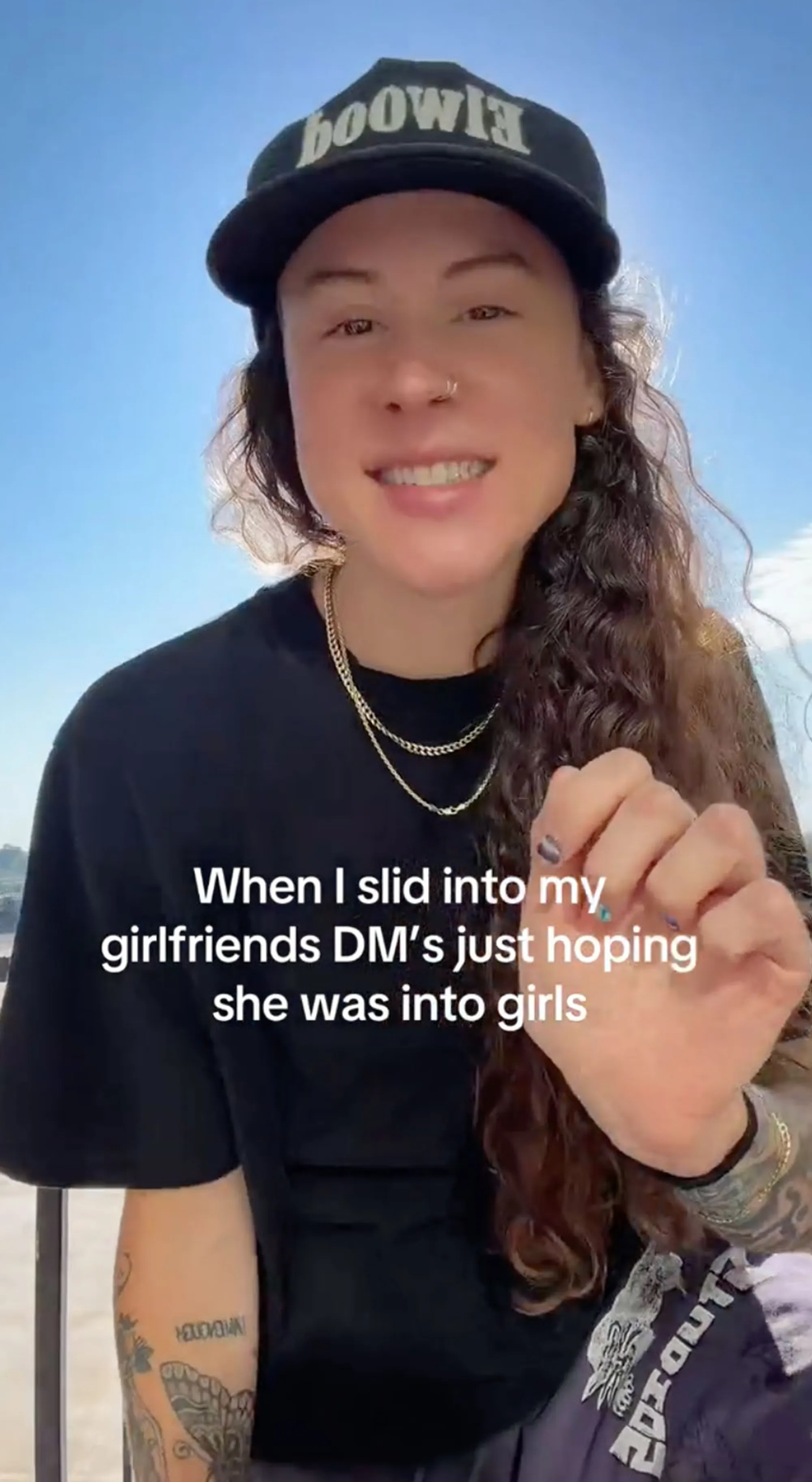 A woman in a black baseball cap and gold chain smiling, with text overlay: 