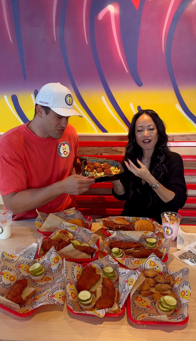 Kris Humphries serving a plate of chicken to a woman, with multiple plates of chicken tenders and sliders on the table.