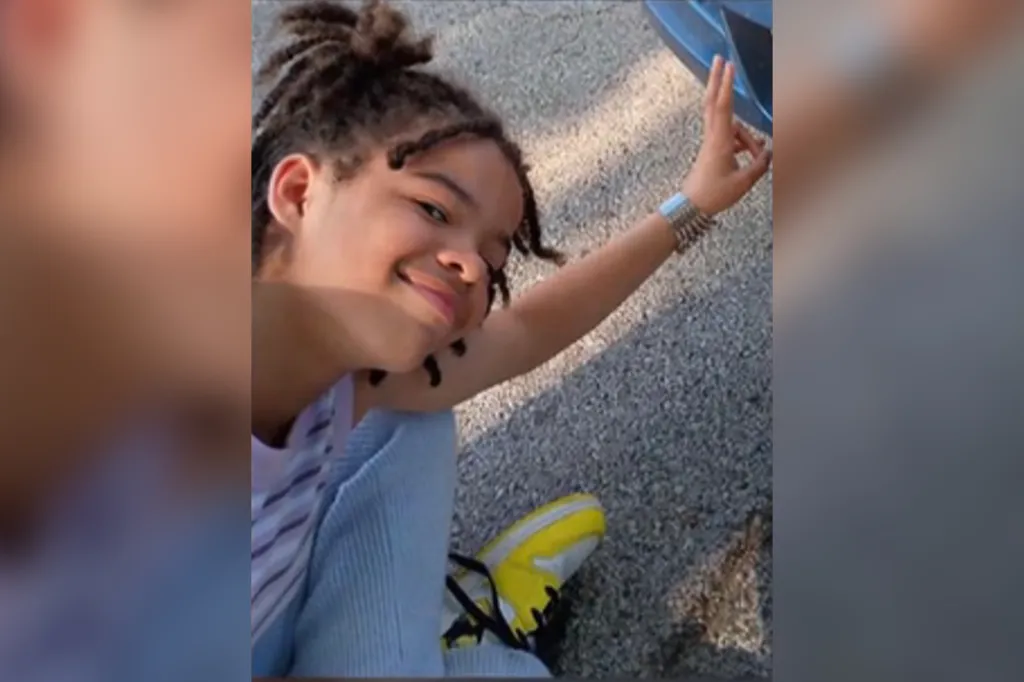 Angelique Cunningham, a young girl with dreadlocks, smiles at the camera, wearing a striped top, light blue overalls, and yellow and black sneakers.