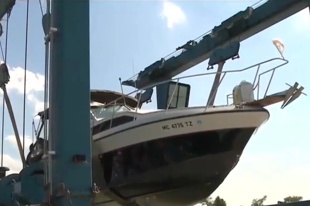 A boat being lifted from the water by a large blue crane, with "MC 4776 TZ" on its bow.