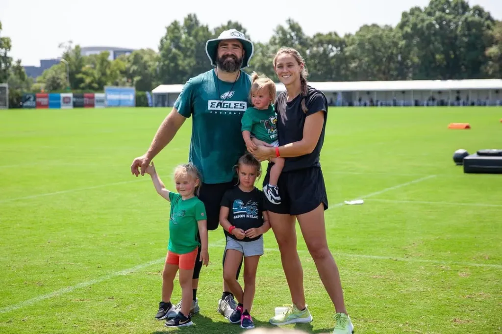 Kylie Kelce, Jason Kelce, and their three daughters posing on a football field.