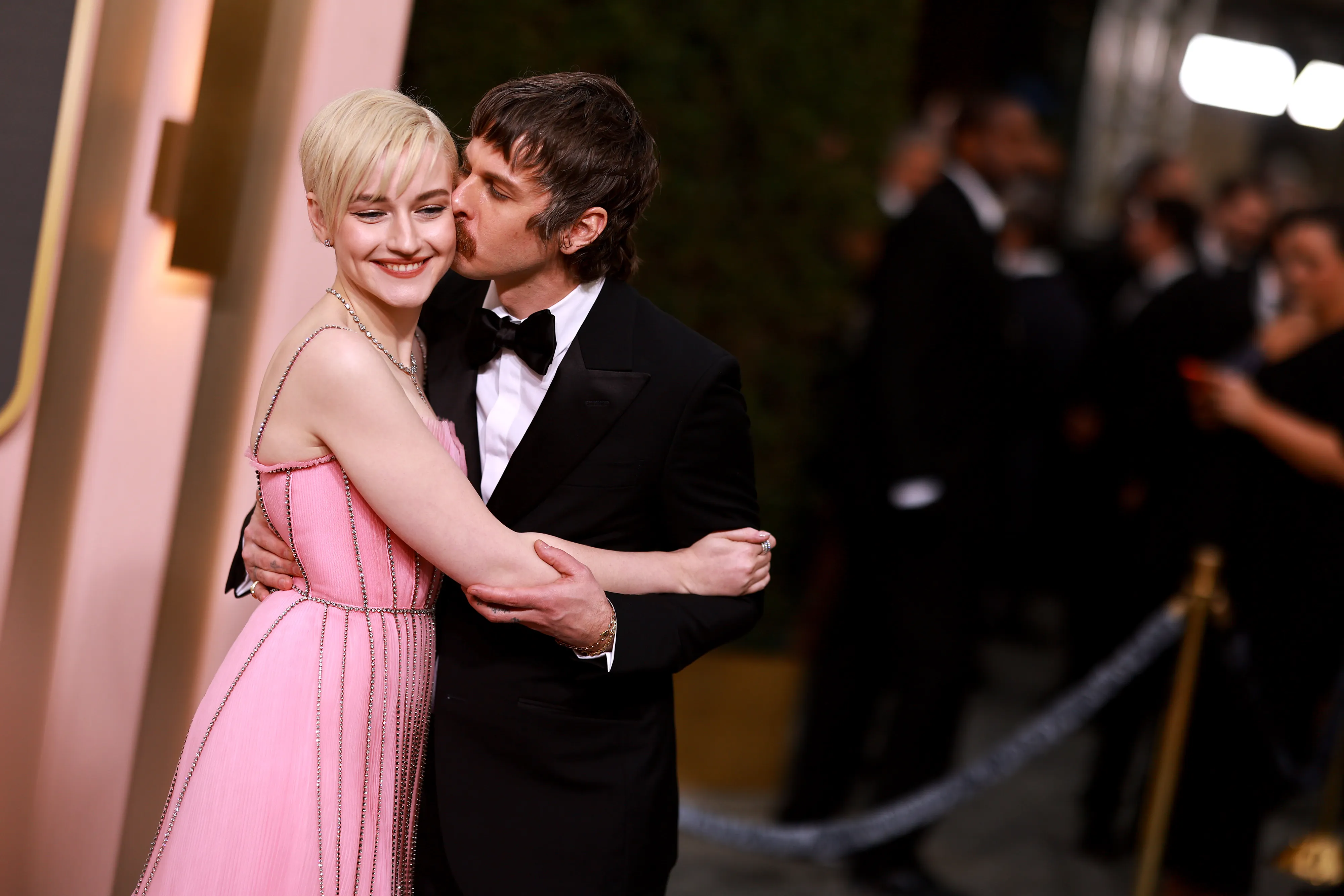 Julia Garner in a pink gown with Mark Foster kissing her cheek.