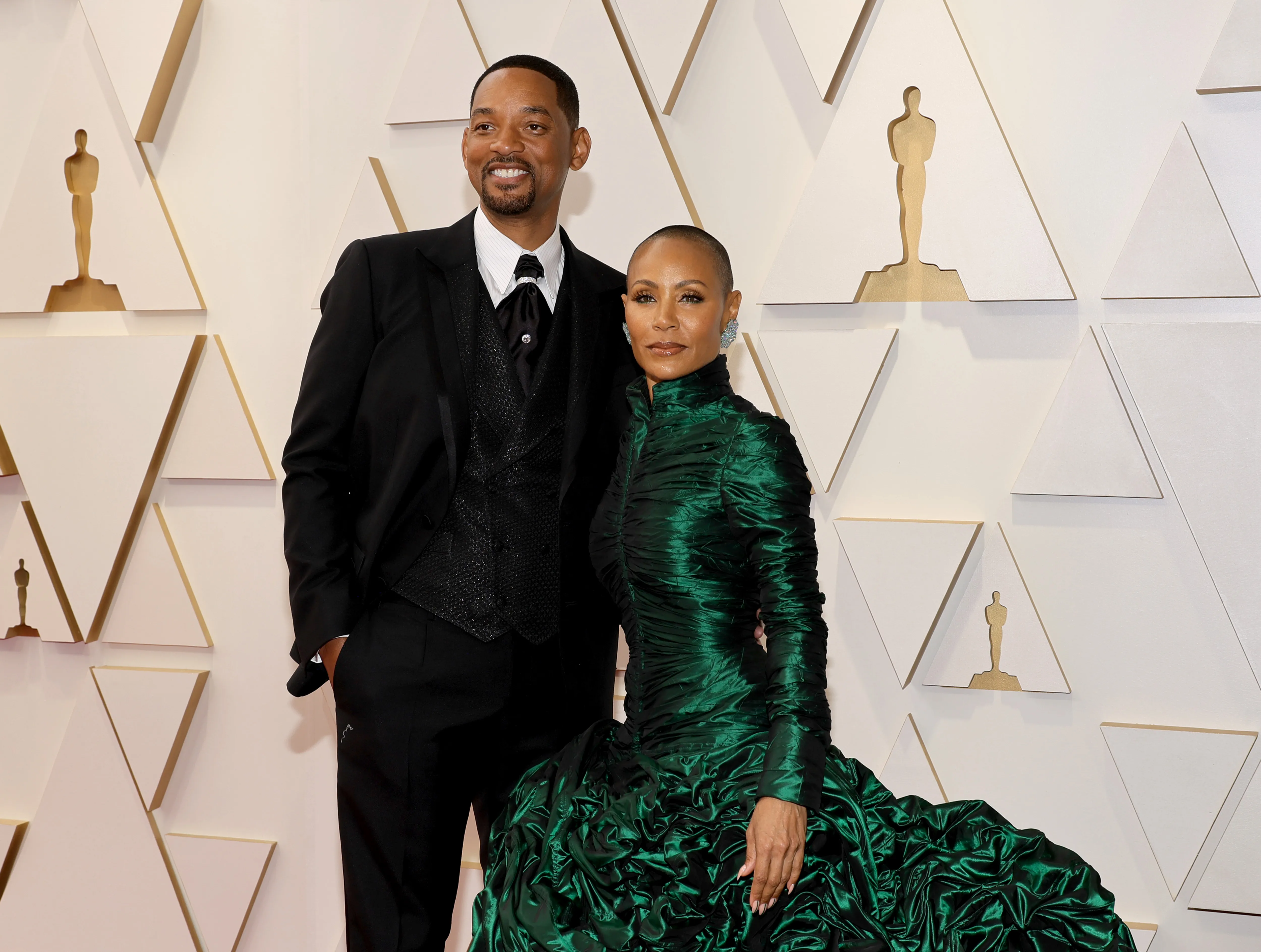 Will Smith and Jada Pinkett Smith posing on the red carpet with Oscar statue cutouts behind them.