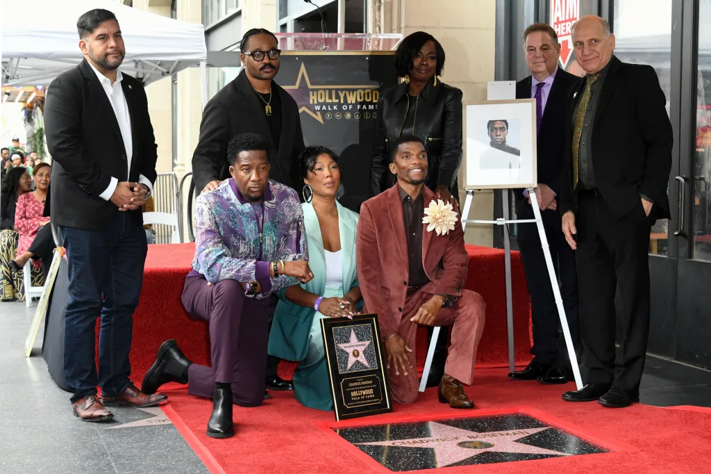 People pose next to Chadwick Boseman's posthumous Hollywood Walk of Fame star, with his brothers Derrick and Kevin Boseman and widow Taylor Simone Ledward kneeling beside it.