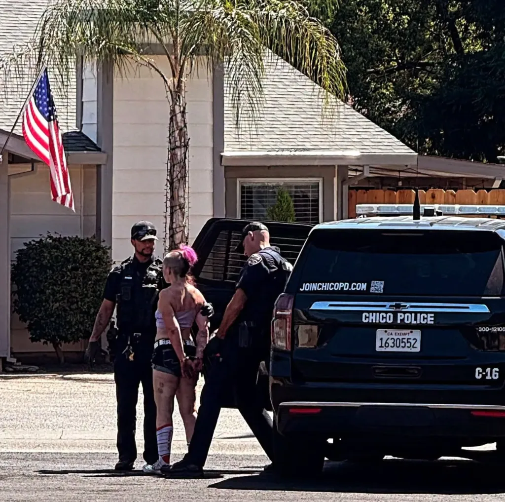 Lacey Roberts in handcuffs, surrounded by two police officers next to a Chico Police vehicle.