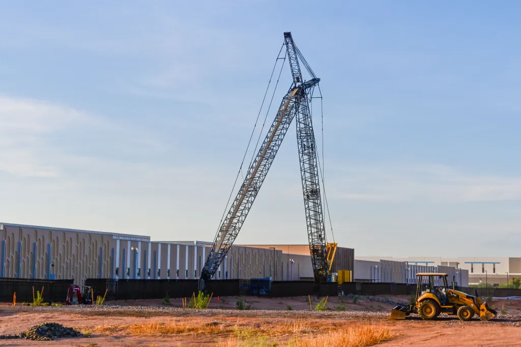 A large data center campus under construction in Mesa, Arizona, featuring a crane, a backhoe, and buildings.