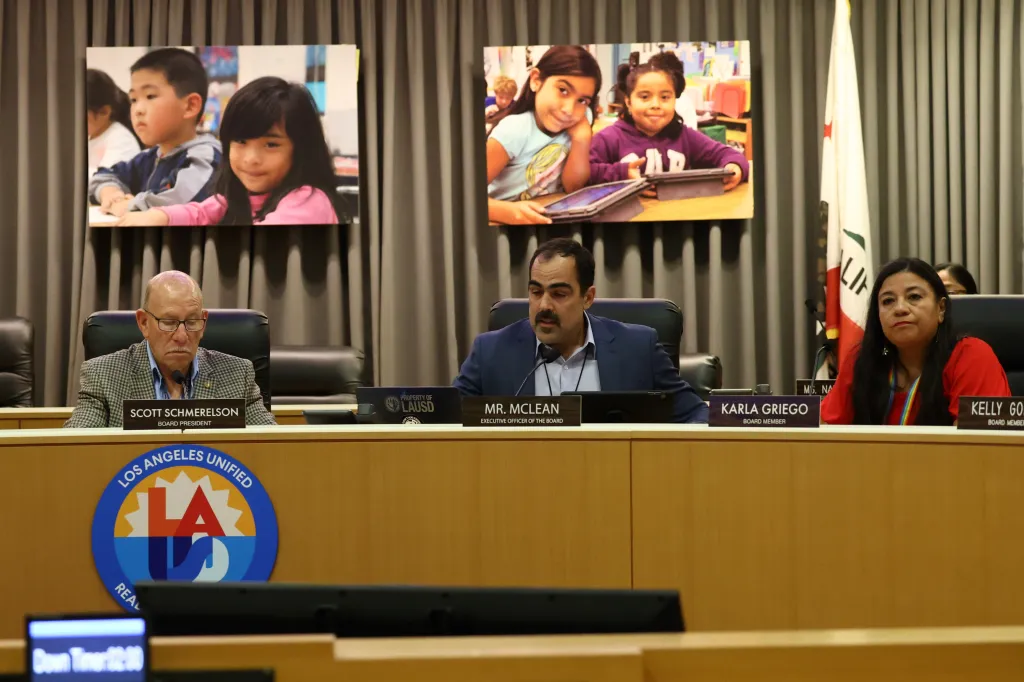 LAUSD School Board meeting with three board members seated at a wooden desk under images of children.