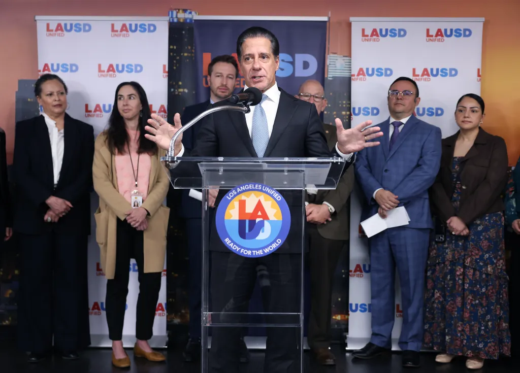 LAUSD Superintendent Alberto Carvalho speaks at a podium surrounded by LAUSD leadership.