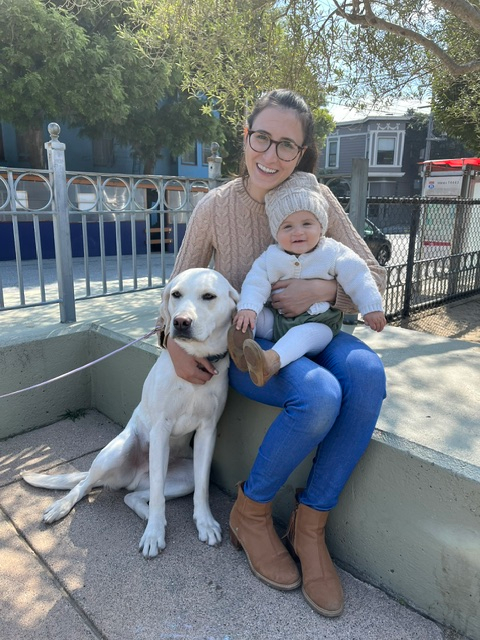 Woman holding a baby and sitting next to a dog