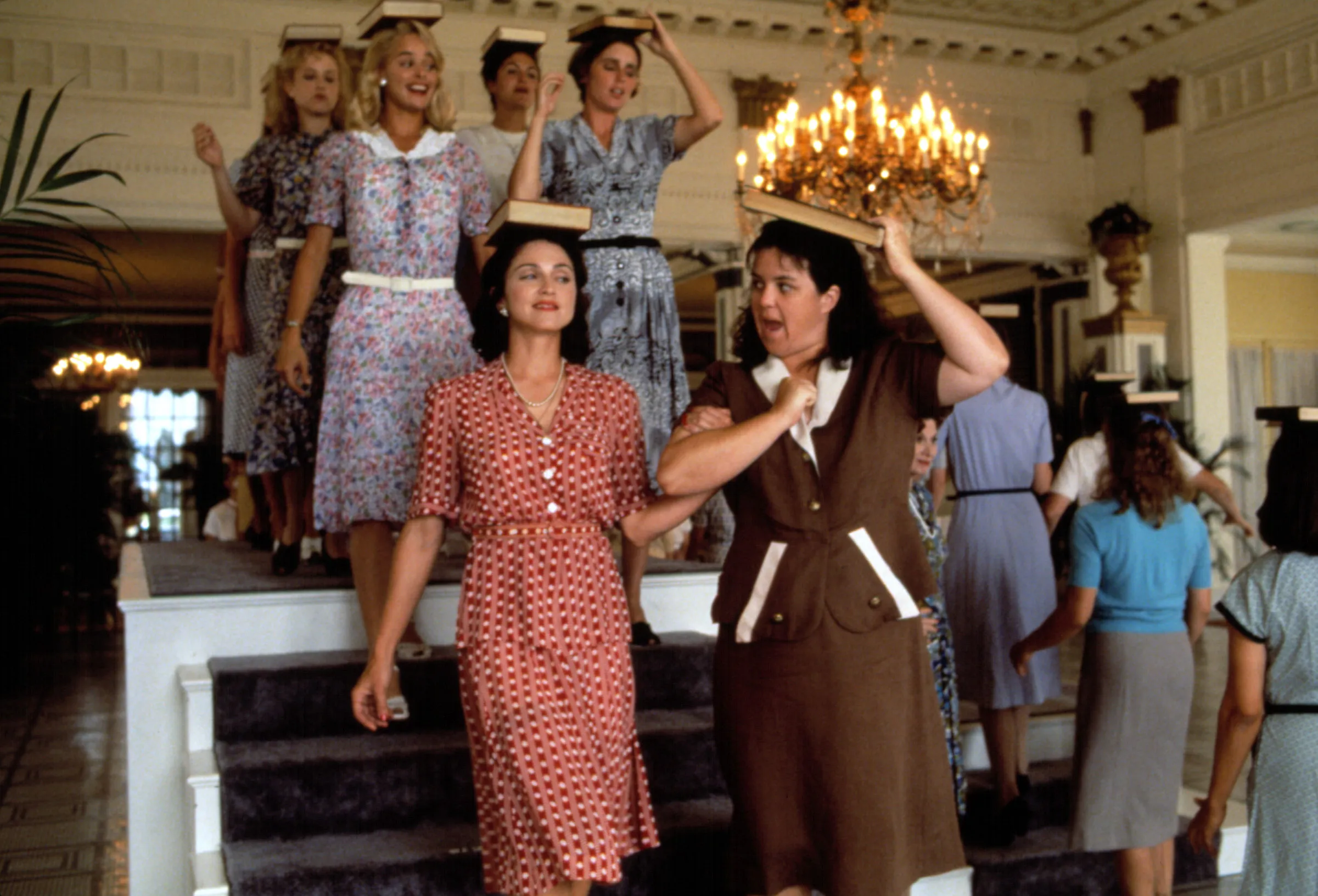 Madonna and Rosie O'Donnell with other women balancing books on their heads on a staircase from