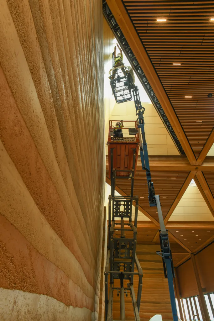 Workers in a lift installing materials on a high wall in the Teddy Roosevelt Presidential Library under construction.