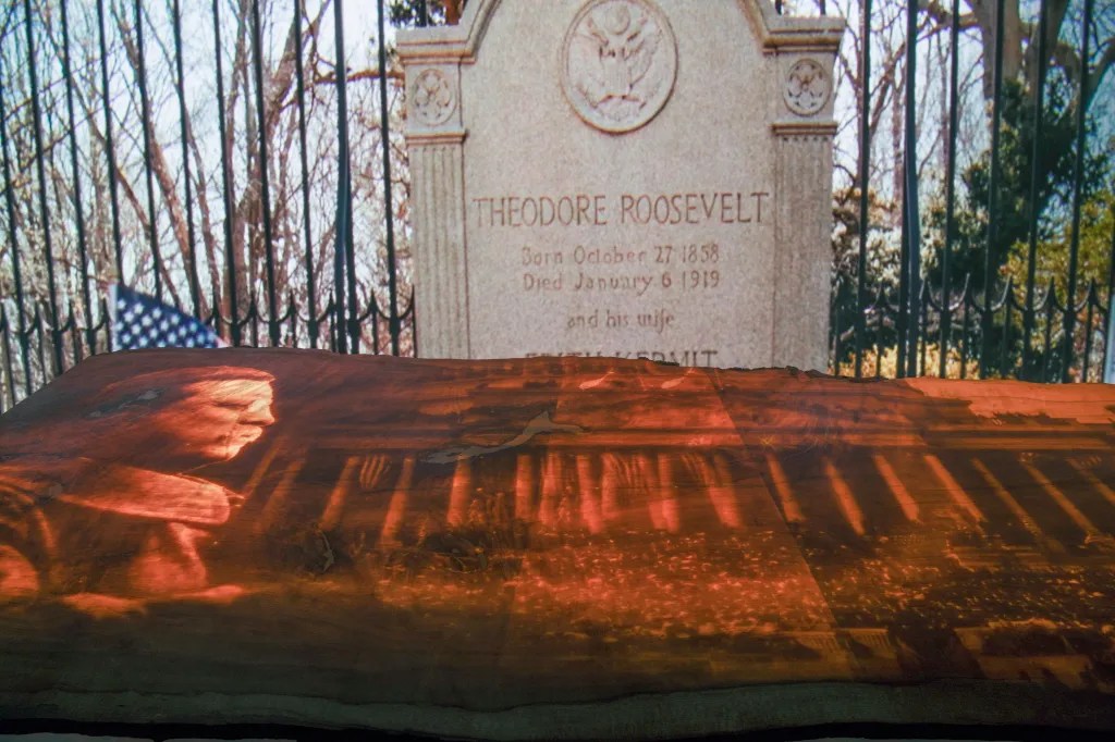 An illuminated display of Theodore Roosevelt's headstone on a table, in front of a fence and an American flag.