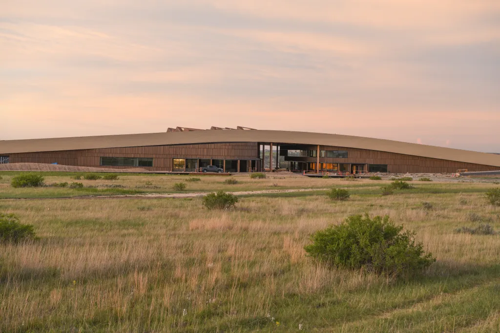 Exterior of the Teddy Roosevelt Presidential Library in Medora, North Dakota, featuring a modern, long, and low-profile building with wooden siding and large windows, surrounded by natural grasslands under a soft, twilight sky.