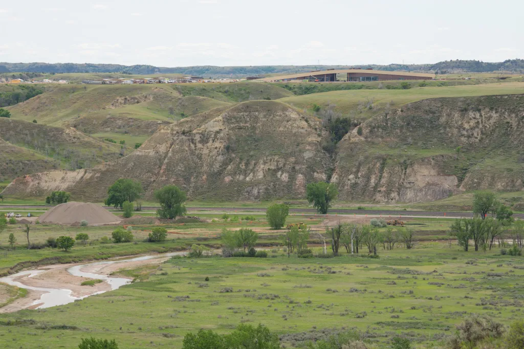 Exterior of the Teddy Roosevelt Presidential Library under construction in Medora, North Dakota, seen from a distance across a valley.