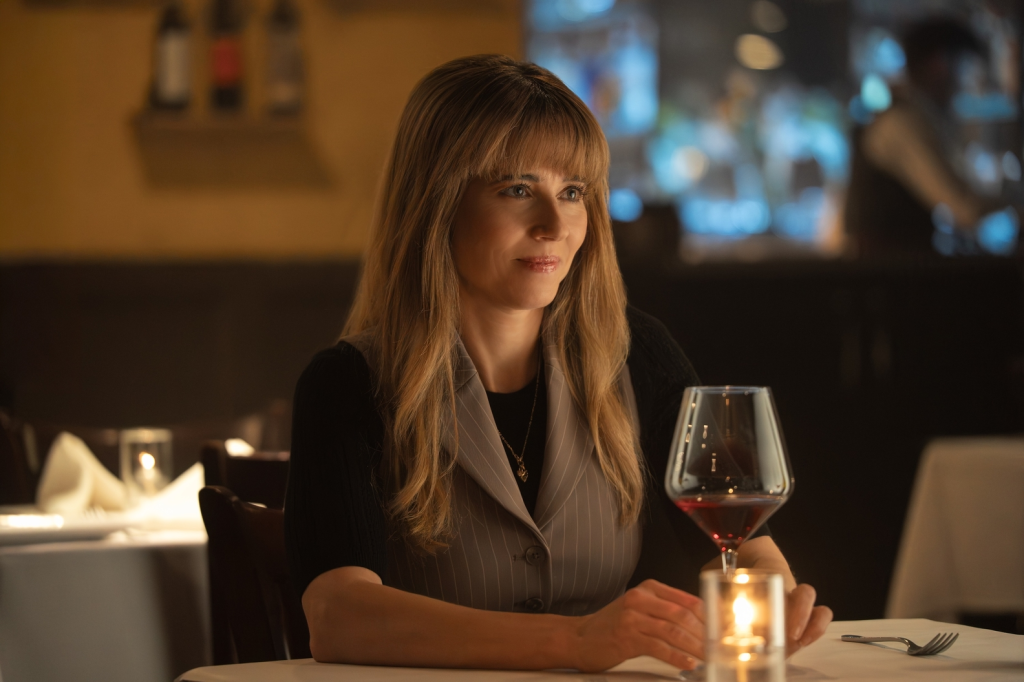 Linda Cardellini at a dining table with a glass of red wine.