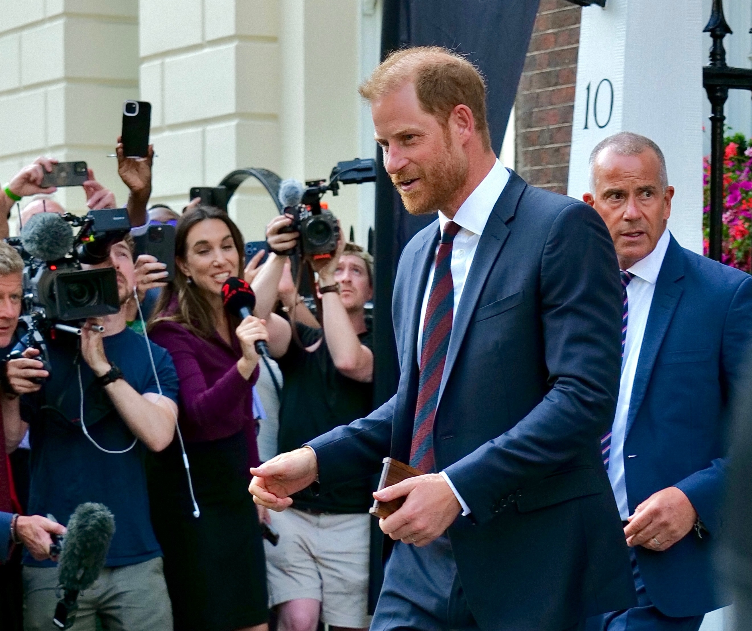 Prince Harry leaving Chatham House in London, surrounded by cameras and reporters.