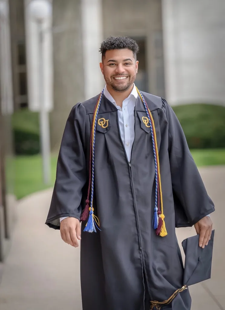 A man in a graduation gown smiles at the camera.