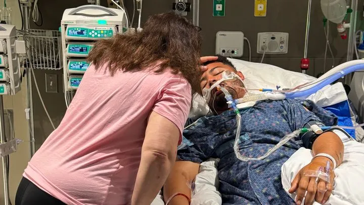 Lonn Hartman in a hospital bed with a woman leaning over him.